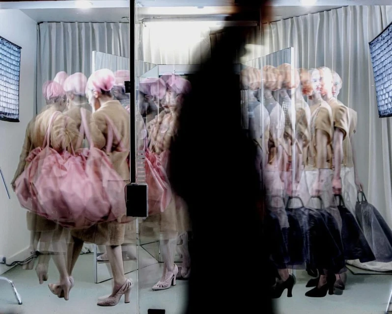 Fashion photography with model in beige outfit and pink accessories reflected in mirrors creating multiple images of the same woman.