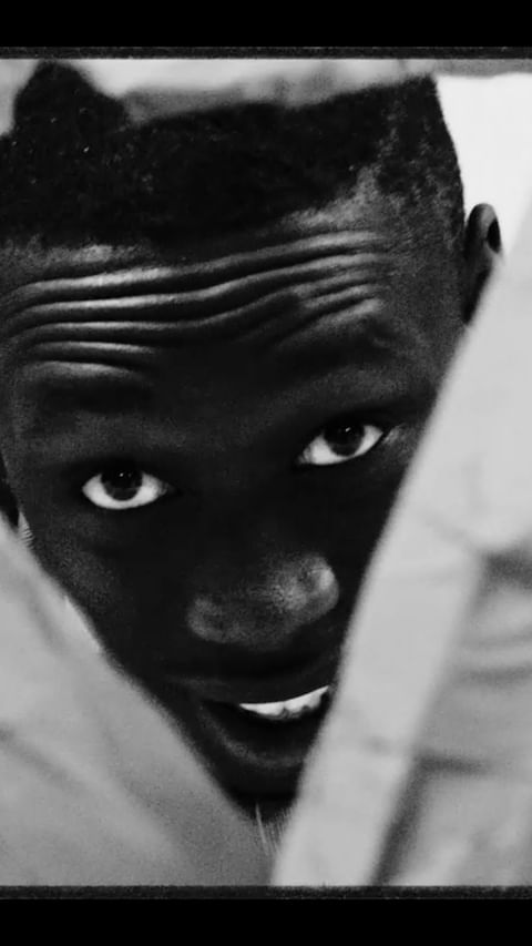 Close-up portrait of an adult African male with a serious expression. The image is black and white, showcasing facial details.