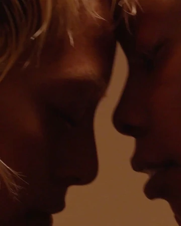 Close-up of two adult humans face-to-face in a dimly lit setting with warm tones, showing their noses and lips, possibly in a moment of intimacy.