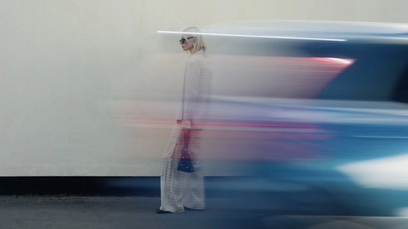 Model standing against a wall with a blurred vehicle passing in the foreground captured in motion
