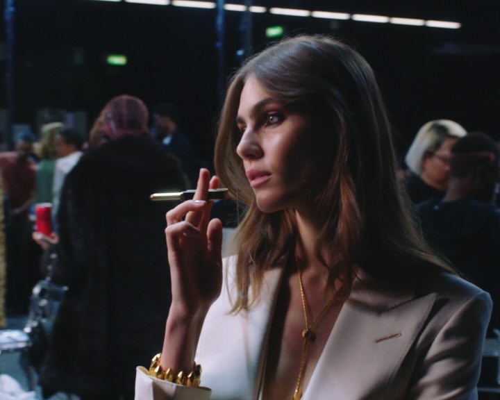 Elegant woman in a white blazer holds a pen, showcasing style and sophistication against a blurred backdrop, emphasizing fashion and beauty.
