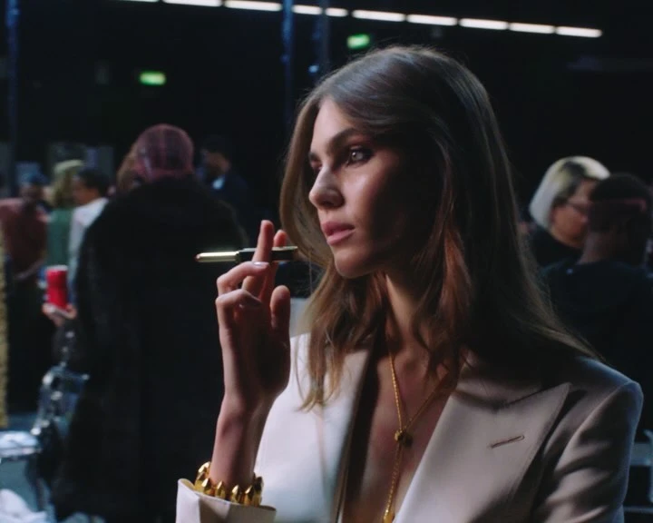 Elegant woman in a white blazer holds a pen, showcasing style and sophistication against a blurred backdrop, emphasizing fashion and beauty.