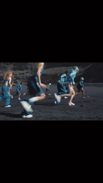 Group of people running on a black sand beach near a rocky hill, captured in motion with blurred legs and sporty fashion attire.