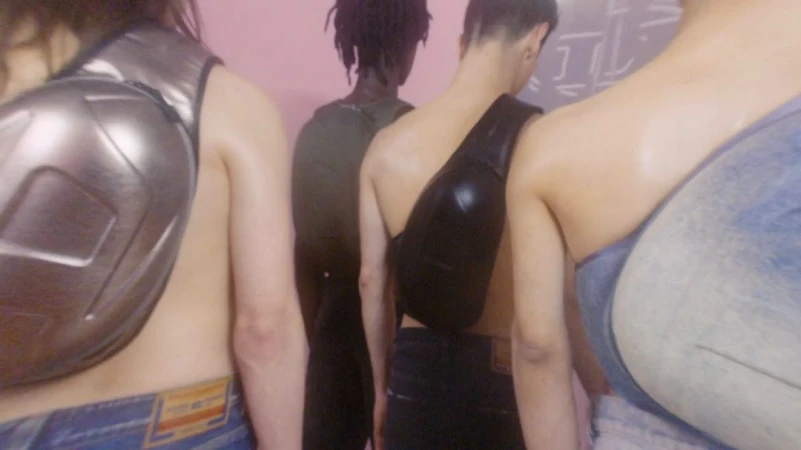 Four models from behind wearing crossbody bags and denim jeans against a plain pink wall
