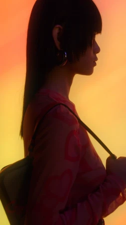 Profile portrait of a woman wearing a patterned top and carrying a shoulder bag against a warm gradient background