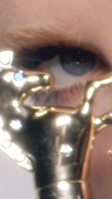 Close-up of an eye with gold decorative horse eye adornment featuring a blue jewel accent, creating a unique and eye-catching detail.