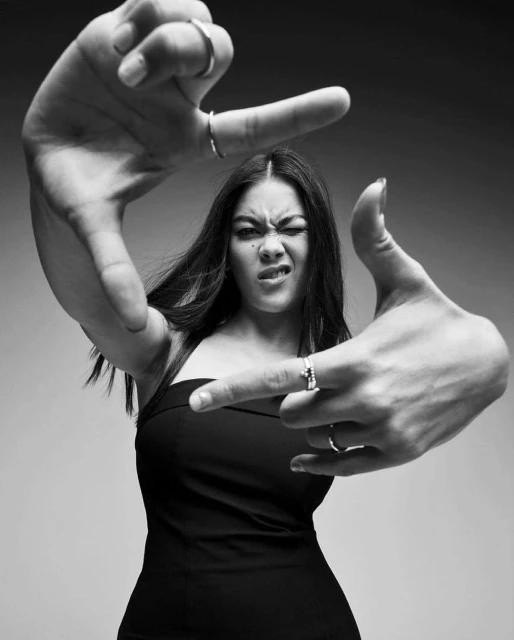 Portrait of a woman in a black dress making a frame with her fingers, creating a dynamic composition with a neutral background in black and white.