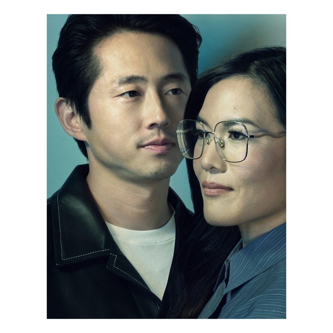 Close up studio portrait of an Asian man and woman posing, the woman wearing glasses, shot against a solid cyan-blue background.