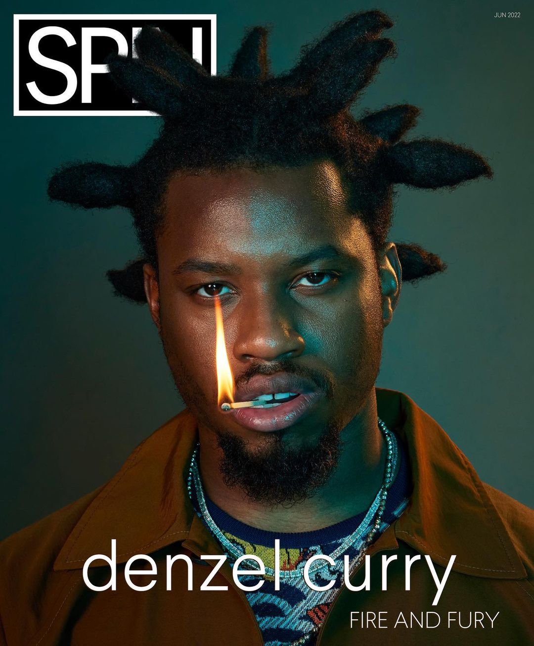 Denzel Curry poses with a match in his mouth on the cover of SPIN magazine, captured in a medium shot with moody, teal-toned lighting.