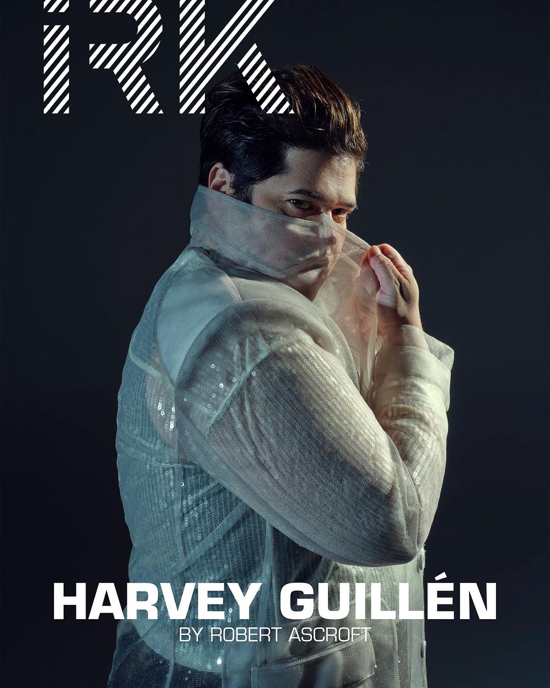 Portrait of Harvey Guillén on a magazine cover with bold typography and a semi-transparent jacket, set against a dark background.
