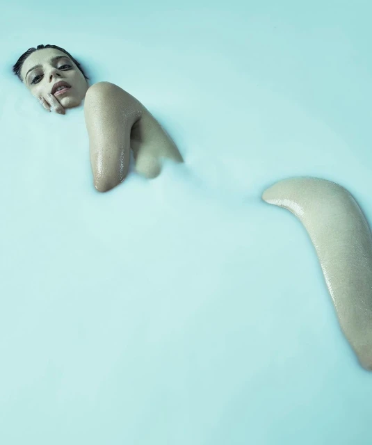 Portrait of a woman partially submerged in a light blue liquid, focusing on her face and upper body, evoking a serene mood.