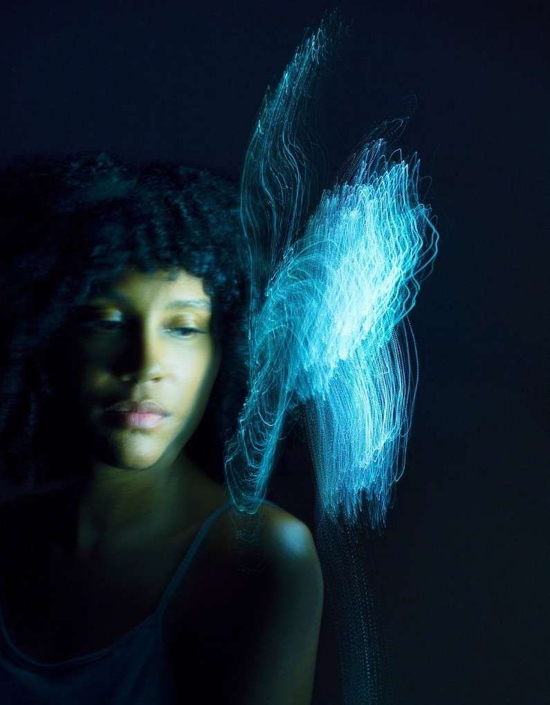 Portrait of a woman with dark curly hair and blue light painting on a dark background, artistic photography, creative lighting.