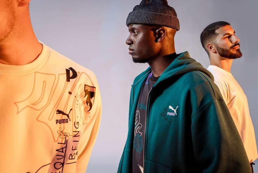 Three men pose in a studio wearing Puma branded sweatshirts and a hoodie, medium shot, studio lighting, neutral background.