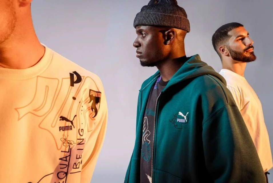 Three men pose in a studio wearing Puma branded sweatshirts and a hoodie, medium shot, studio lighting, neutral background.