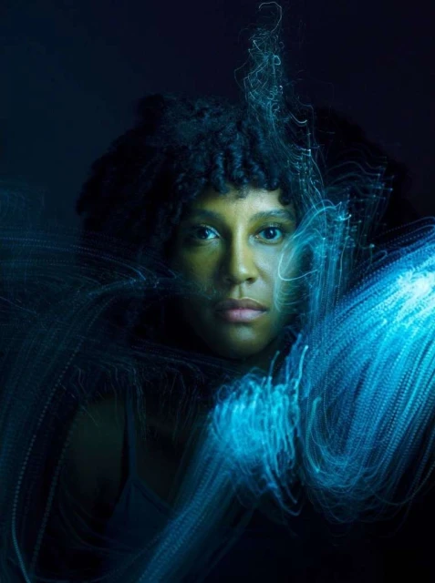 Portrait of a woman with glowing blue light streaks surrounding her face against a dark backdrop, creating a visually stunning effect.