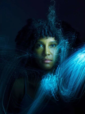 Portrait of a woman with glowing blue light streaks surrounding her face against a dark backdrop, creating a visually stunning effect.