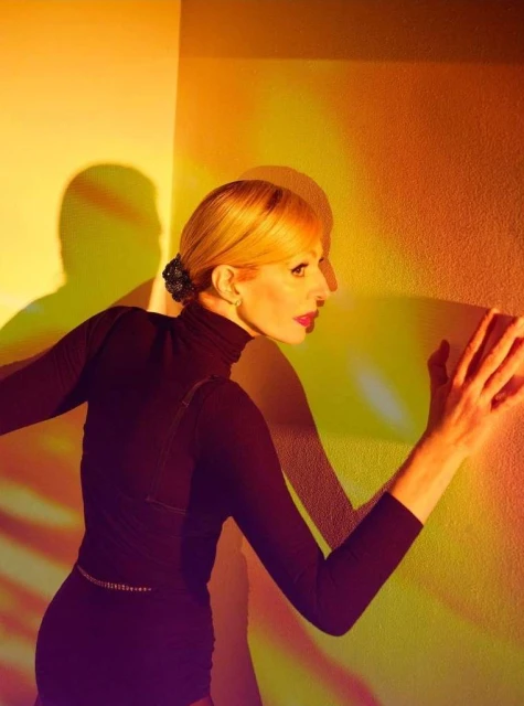 Woman in turtleneck dress strikes a dynamic pose against a vibrant wall with interesting shadows creating a striking visual impact.