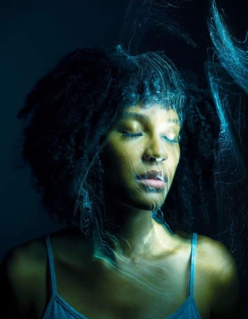 Close-up portrait of an African-American woman with closed eyes, dark hair, and a blue tank top, with soft blue light painting effect.