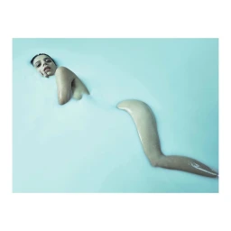Woman submerged in milky blue liquid with her head and leg visible above the surface, photographed by Robert Ascroft.