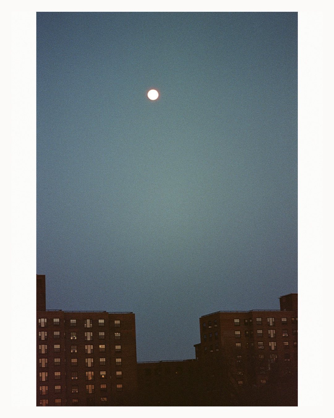 Full moon over urban apartment buildings, casting a serene and calming light across the cityscape at twilight or dusk.