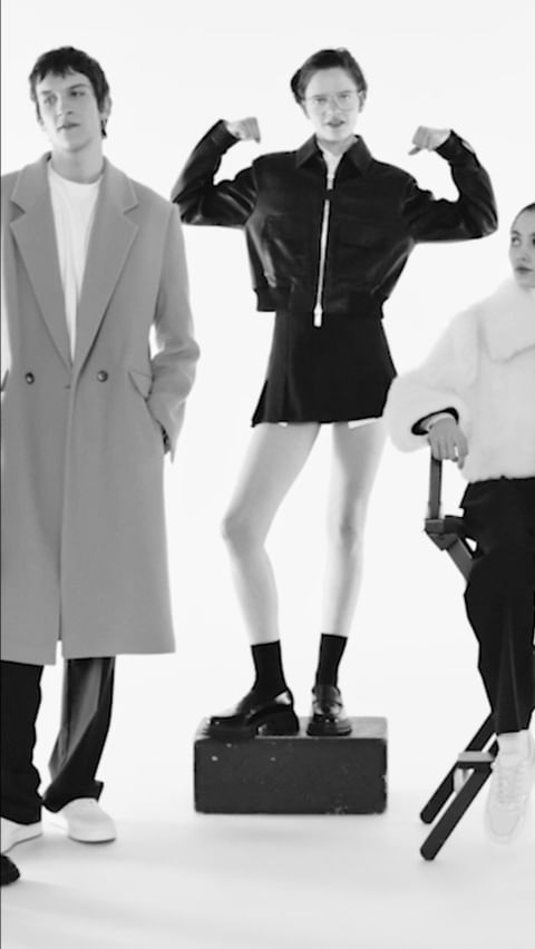 Black and white fashion shot featuring three stylish adults in a minimalist studio setting, showcasing contemporary clothing and posing. 