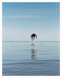 A person diving headfirst into calm blue ocean water with a clear horizon under a bright sky, photographed by Robert Nethery.