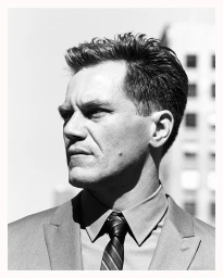 Monochrome portrait of a man in a suit and striped tie looking away against an outdoor architectural background.