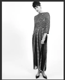 Model in patterned checkered dress and black heels standing against a bright white seamless background.