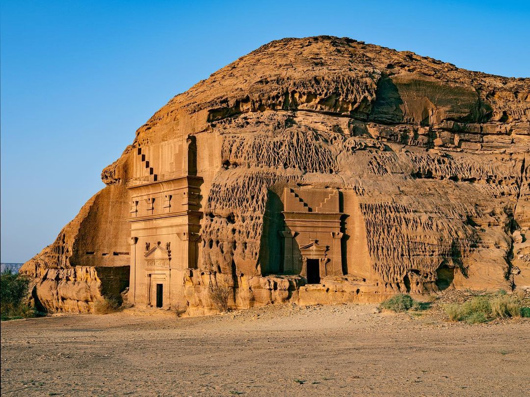 Ancient Nabataean tomb architecture carved into a sandstone mountain with blue sky in the Al-Ula region of Saudi Arabia.