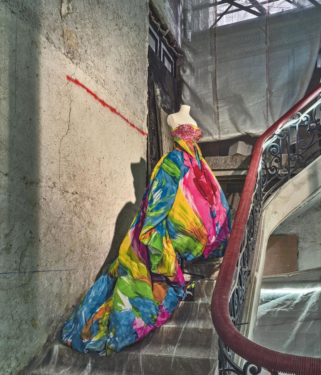 Colorful dress on a mannequin, placed on stairs in an indoor setting, against a concrete wall with a red stripe.