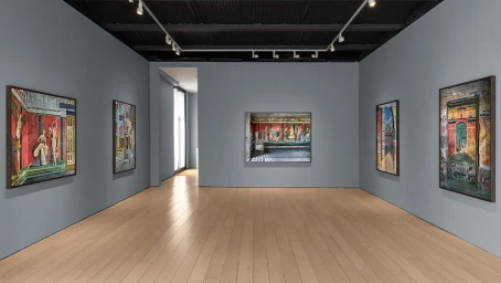 Wide shot of an art gallery interior with grey walls, light wood floors, and several framed photographs hanging on display.