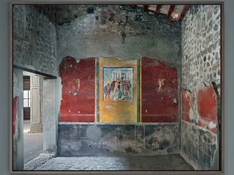 Interior shot of an ancient stone room with vibrant red and yellow frescoes on the central wall by Robert Polidori.