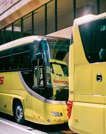 Two yellow buses parked side-by-side near a modern building, showcasing transportation and urban design.