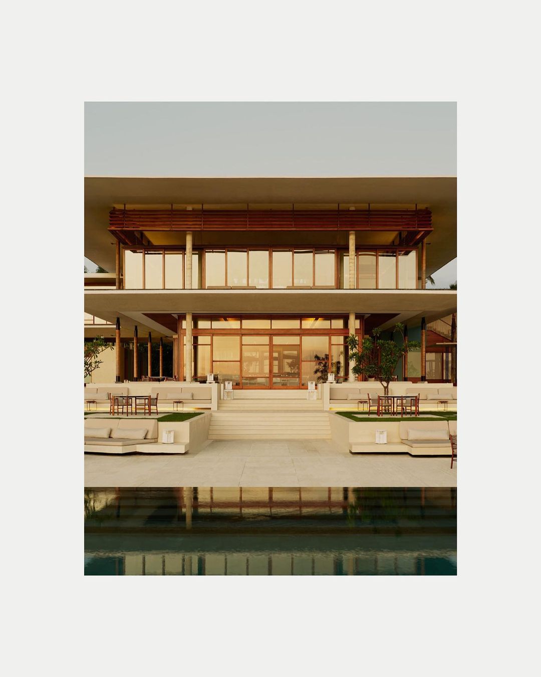Exterior view of a modern two-story building with a flat roof, outdoor seating, and a swimming pool in front, showcasing contemporary architecture.