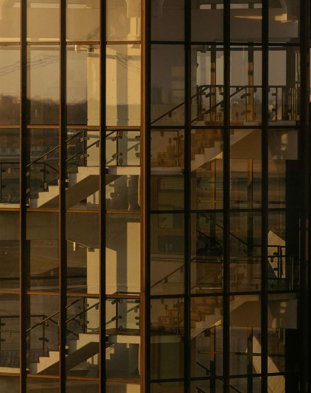 Architectural shot of a modern building with glass windows and a staircase, warm light reflecting on the structure, creating a geometric pattern.