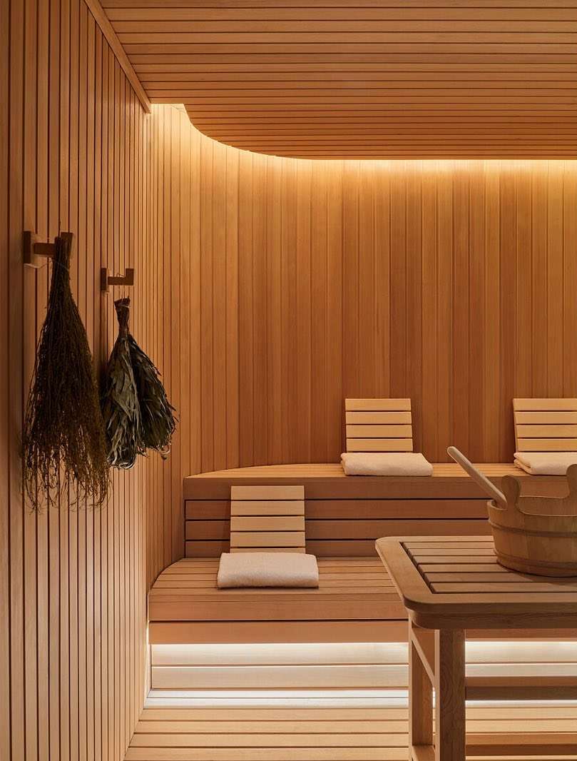 Interior of a wooden sauna room with benches, a bucket with a ladle, and besoms hanging on the wall, creating a warm and relaxing atmosphere.