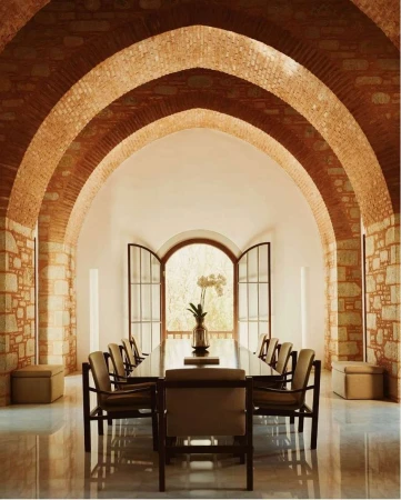 Indoor dining area featuring a long table with chairs, brick arches, and an open window, creating a bright and inviting space.