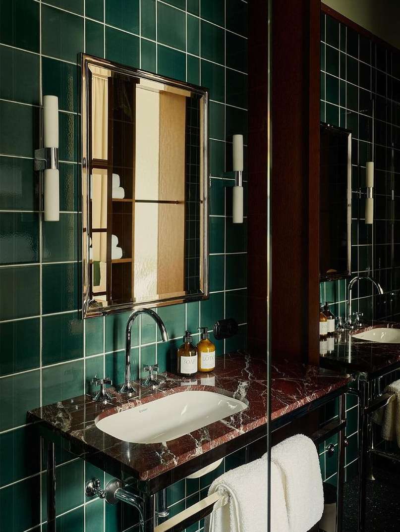 Modern bathroom features a white sink with chrome fixtures, a red marble countertop, green tiled walls, and a large mirror.