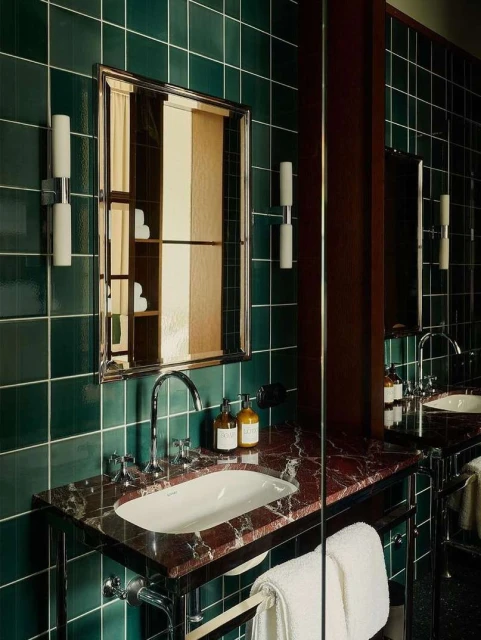 Modern bathroom features a white sink with chrome fixtures, a red marble countertop, green tiled walls, and a large mirror.