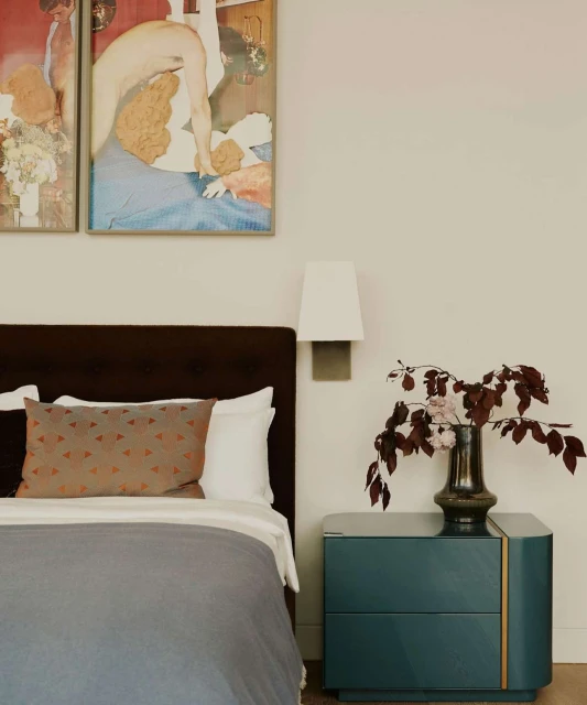 Modern bedroom interior featuring a bed with a gray duvet, brown headboard, and a bedside table with a vase of burgundy flowers.