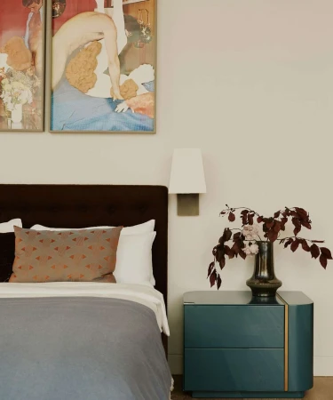 Modern bedroom interior featuring a bed with a gray duvet, brown headboard, and a bedside table with a vase of burgundy flowers.