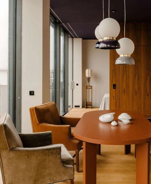 Interior view showcases a modern dining room with brown chairs around an orange table, pendant lights, and large windows.