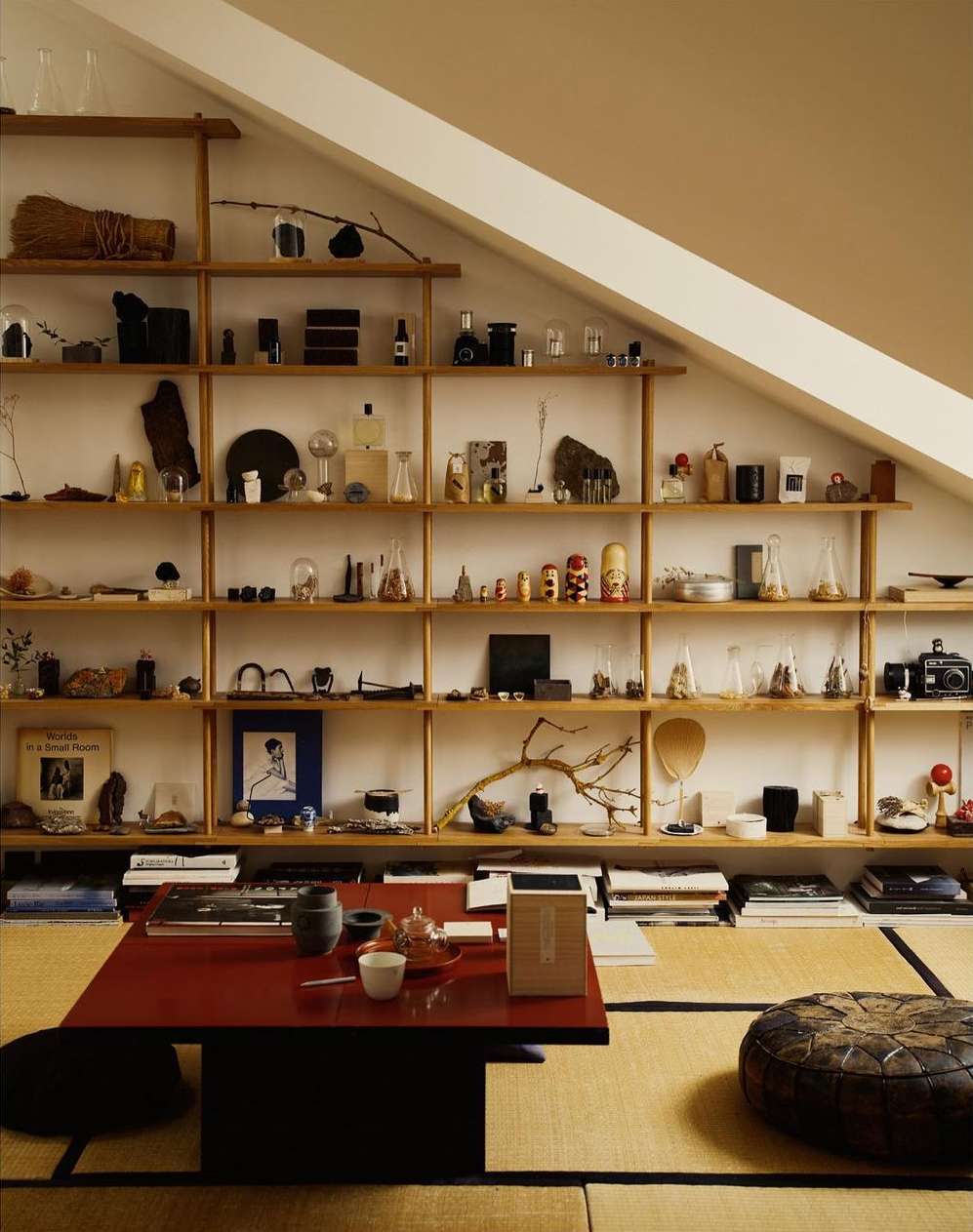Attic room interior features wooden shelves with assorted objects, low table with tea set, and floor cushions on tatami mats.