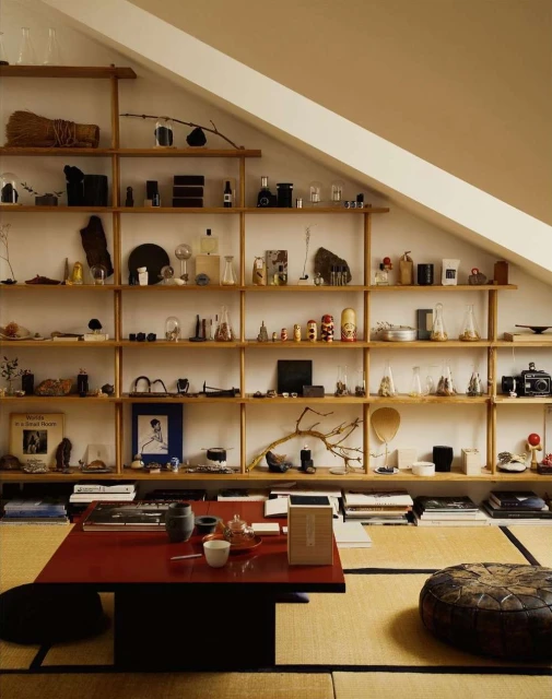 Attic room interior features wooden shelves with assorted objects, low table with tea set, and floor cushions on tatami mats.