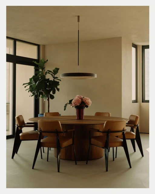 Interior of a dining room with a round wooden table surrounded by six leather and black chairs, underneath a modern pendant light.