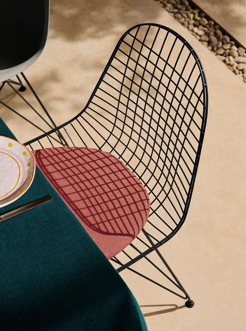 Outdoor dining scene featuring a black wire chair with a red cushion, table with a dark green tablecloth, plate and flatware on a patio.