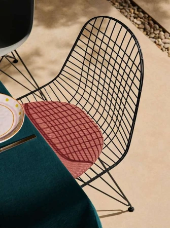 Outdoor dining scene featuring a black wire chair with a red cushion, table with a dark green tablecloth, plate and flatware on a patio.
