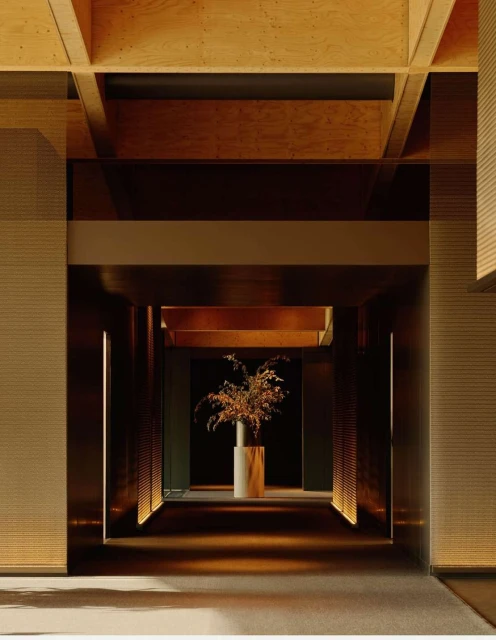 Interior view of a corridor with dark metal walls, a cylindrical vase with branches, and wooden ceiling beams, creating depth and architectural interest.