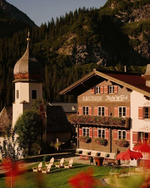 View of the Gastof Rote Wand building and adjacent church in a mountain valley, with timber construction and grassy lawn.