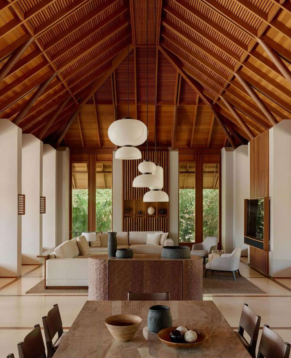 Modern interior with vaulted wood ceiling, globe pendant lights, neutral furniture, wood table, and view to outdoor greenery.